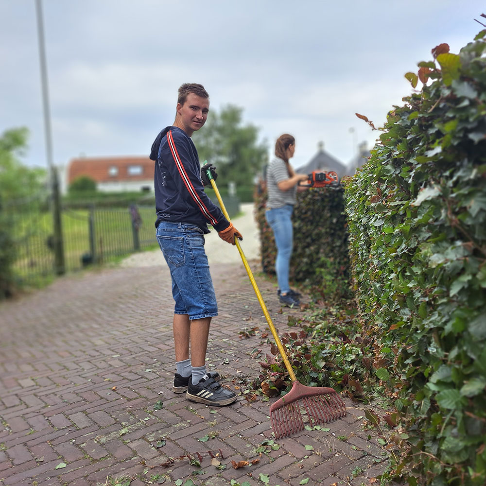 Een man en vrouw zijn bezig met het snoeien van een haag in een tuin.