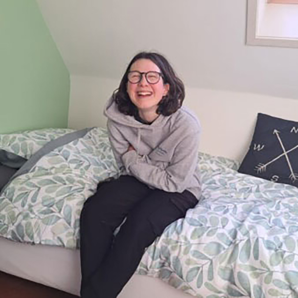 Een vrouw zit op een bed in een kamer, omringd door zachte verlichting en een gezellige inrichting.
