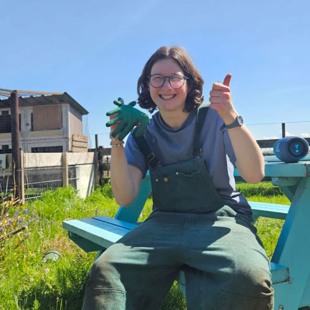 Een vrouw zit op een bank met een groene beker in haar hand, omringd door een groene omgeving.
